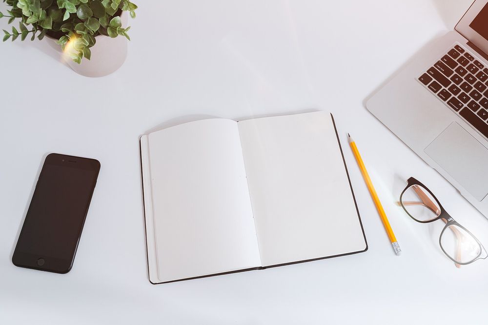 A notebook, pen and laptop on a white desk